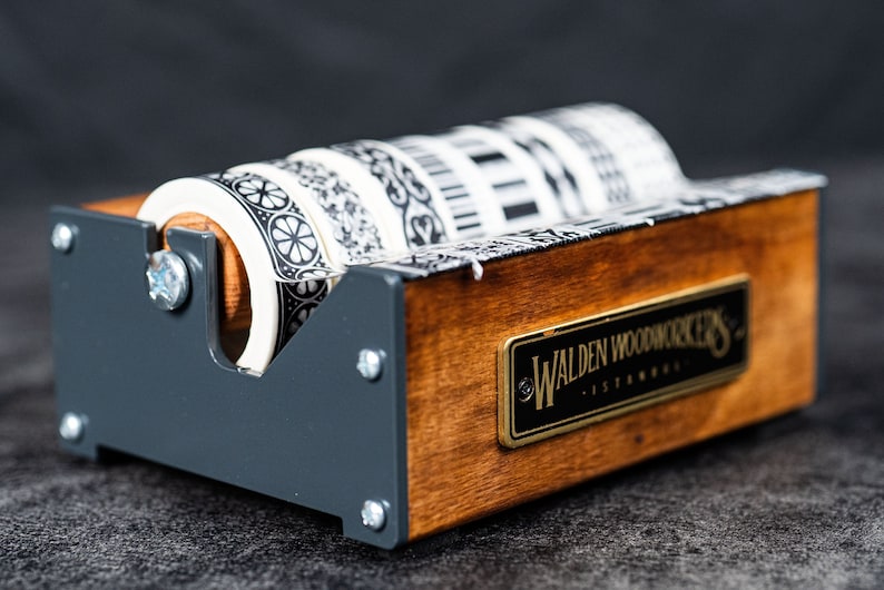 May include: A wooden tape dispenser with a black metal frame and four rolls of black and white patterned tape. The dispenser has a brass plaque that reads "Walden Woodworkers - Established".