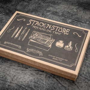 May include: A rectangular pen and ink tray box with the words "STACK-N-STORE PEN AND INK TRAY" printed on the lid. The box is brown with a black top, featuring illustrations of pens, ink bottles, and a pen tray. The box is labeled "Walden Woodworkers" and "Galen Leather Co."