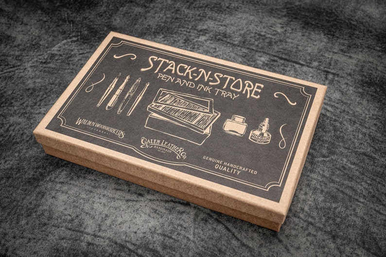 May include: A rectangular pen and ink tray box with the words "STACK-N-STORE PEN AND INK TRAY" printed on the lid. The box is brown with a black top, featuring illustrations of pens, ink bottles, and a pen tray. The box is labeled "Walden Woodworkers" and "Galen Leather Co."