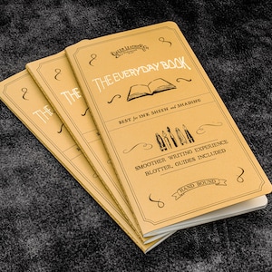 以下が含まれることがあります： 「The Everyday Book」という文字が書かれた黄色のノートが3冊。表紙には、開いた本のイラスト、