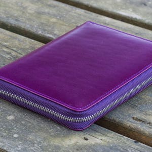 May include: A purple leather zippered wallet or clutch purse. The zipper is silver and the leather is smooth.