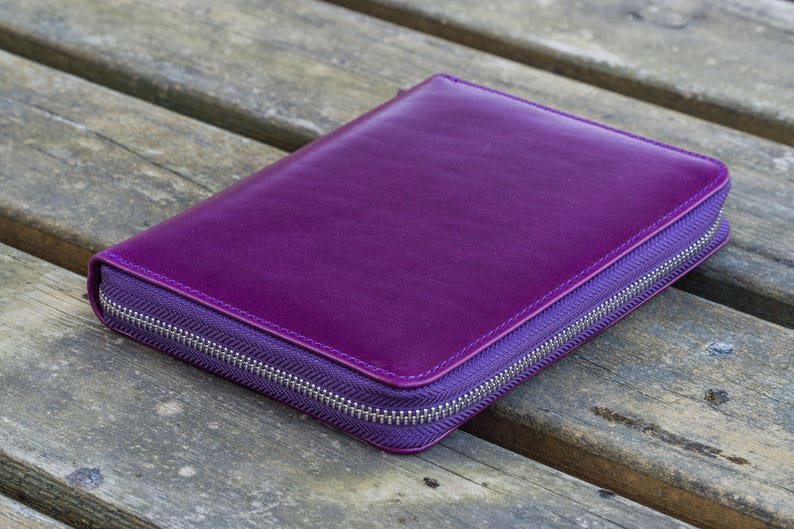 May include: A purple leather zippered wallet or clutch purse. The zipper is silver and the leather is smooth.