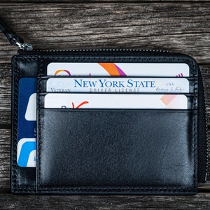 May include: A black leather zippered wallet with a New York State driver's license, a Veteran card, and a credit card inside.