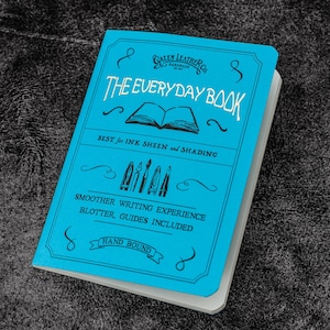Pu&ograve; includere: Un quaderno blu con il testo "GALEN LEATHER CO. HANDMADE GOODS" e "THE EVERYDAY BOOK" sulla copertina anteriore. Il testo "BEST for INK SHEEN and SHADING" &egrave; anche sulla copertina. Il quaderno &egrave; rilegato a mano e include un assorbi inchiostro e guide.