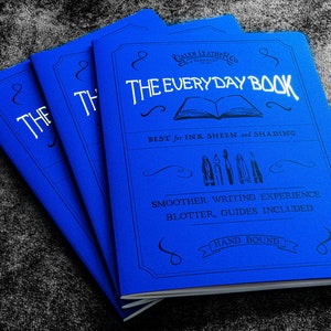 Könnte beinhalten: Drei blaue Notizbücher mit dem Text "Galen Leather Co. The Everyday Book" auf dem vorderen Umschlag. Der Text "Best for Ink Sheen and Shading" befindet sich unter dem Titel. Der Text "Smoother Writing Experience, Blotter, Guides Included" befindet sich unter der ersten Textzeile. Der Text "Hand Bound" befindet sich in einem Banner am unteren Rand des Umschlags.