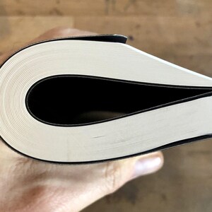 K&ouml;nnte beinhalten: Nahaufnahme des Buchr&uuml;ckens eines gebundenen Buches mit wei&szlig;en Seiten und einem schwarzen Einband.