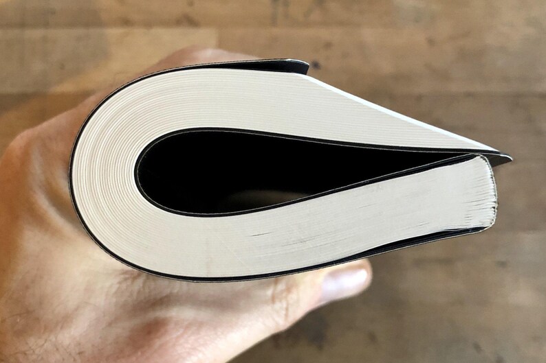 K&ouml;nnte beinhalten: Nahaufnahme des Buchr&uuml;ckens eines gebundenen Buches mit wei&szlig;en Seiten und einem schwarzen Einband.