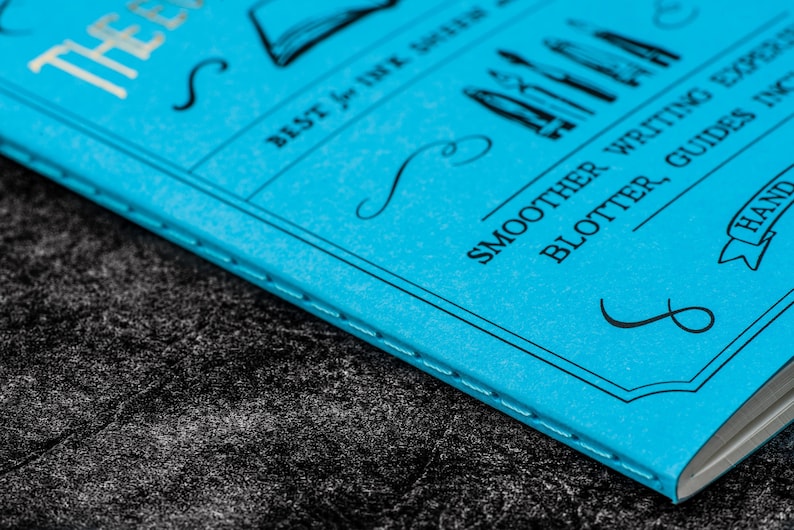 Pu&ograve; includere: Un quaderno blu con il testo "The Ever After" e "Best for Ink & Quill" sulla copertina. Il quaderno ha anche il testo "Smoother Writing Experience, Blotter, Guides Included, Hand Crafted" sulla copertina.