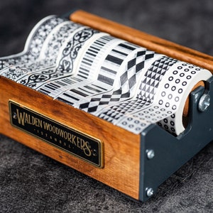 May include: A wooden tape dispenser with a black metal frame holds five rolls of black and white patterned washi tape. The dispenser has a brass plaque that reads "Walden Woodworkers Istanbul."