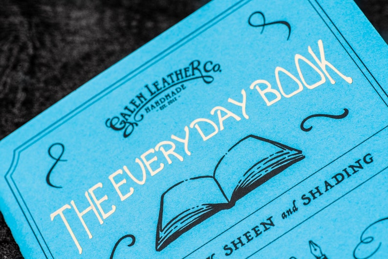 Pu&ograve; includere: Un quaderno blu con il testo "The Everyday Book" in lettere bianche. Il quaderno &egrave; di Galen Leather Co. e presenta un'illustrazione in bianco e nero di un libro aperto.