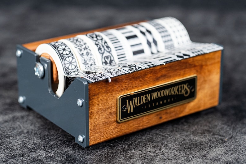 May include: A wooden tape dispenser with black and white patterned tape. The dispenser has a metal frame and a label that reads "Walden Woodworkers - Istanbul".