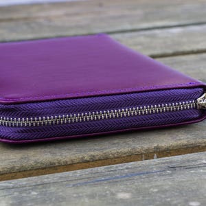 May include: A purple leather zippered wallet or clutch purse with a silver zipper.