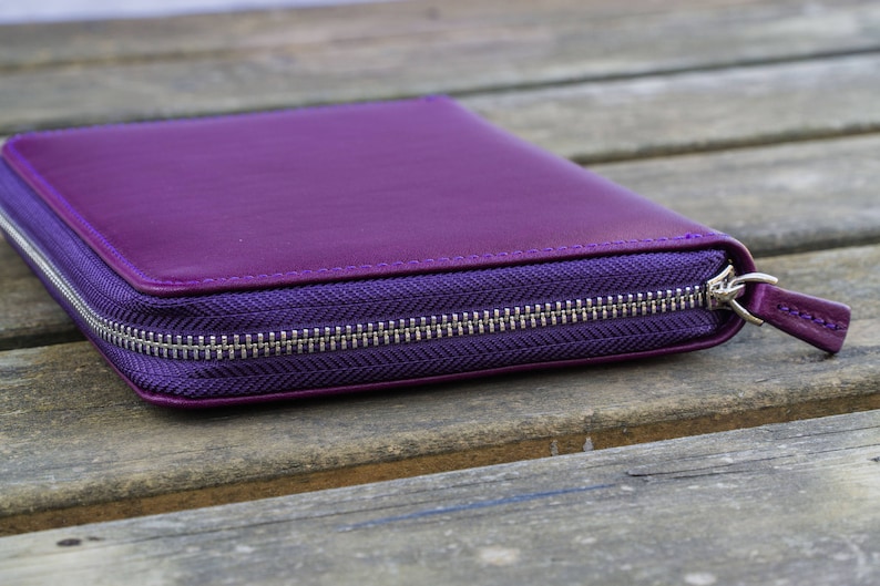 May include: A purple leather zippered wallet or clutch purse with a silver zipper.