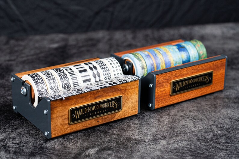 May include: Two wooden tape dispensers with black metal accents. Each dispenser holds multiple rolls of patterned washi tape. The dispensers have a brass plaque with the text "Walden Woodworkers Istanbul".