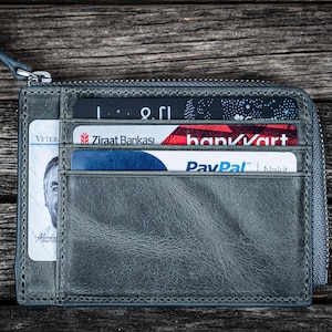May include: A gray leather zippered wallet with multiple cards inserted. The cards include a Ziraat Bankası card, a bank/kort card, and a PayPal card.
