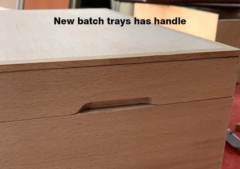 May include: Close-up of a light-colored wooden box with a recessed handle. The box has a smooth, natural wood finish and a simple, rectangular design. The text "New batch trays has handle" is visible.