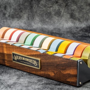 May include: A wooden tape dispenser with a black metal base and a label that reads "Walden Woodworkers - Istanbul". The dispenser holds eight rolls of colorful tape.