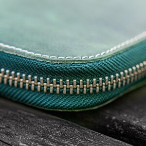 May include: Close-up of a teal zipper on a leather wallet. The zipper is made of metal and has a silver finish.