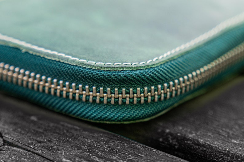 May include: Close-up of a teal zipper on a leather wallet. The zipper is made of metal and has a silver finish.