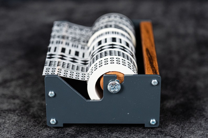 May include: A grey and wood tape dispenser with a white patterned tape roll. The tape has a black and white geometric design.