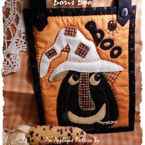 Peut inclure: Un modèle d'appliqué pour une décoration d'Halloween appelée "Boris Boo". Le motif représente une citrouille noire et blanche avec un chapeau de sorcière et le mot "Boo" en feutre noir. Le motif est de Diane Knott LLC.