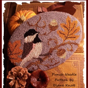 Puede incluir: Un patrón ovalado de aguja perforada con dos carboneros en una rama con hojas de otoño. El diseño es en tonos morado, marrón, naranja y blanco. También hay una pequeña calabaza, una piña y un objeto rojo oscuro.