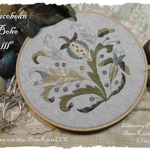 May include: Embroidered hoop art featuring a floral design in shades of green, blue, and white. The design is labelled "Jacobean Boho III" and is credited to Diane Knett LLC. The hoop is surrounded by embroidery floss and scissors.