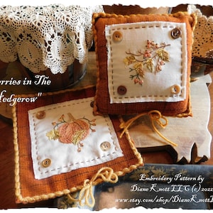 May include: Two embroidered cushion covers with an autumnal theme. One features a pumpkin and the other features berries and leaves. Both are on a brown surface with a crocheted doily in the background. The text "Berries in The Hedgerow" is visible in the image. Embroidery Pattern by Diane Knett LLC (c) 2022 www.etsy.com/shop/Diane Knett LLC