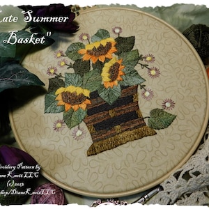 May include: Embroidered hoop art featuring a basket of sunflowers and small white flowers. The text "Late Summer Basket" is at the top of the hoop. The embroidery pattern is by Diane Knett LLC.