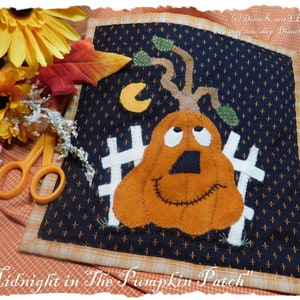 Puede incluir: Una aplicación de fieltro de una calabaza sonriente con una valla y una luna creciente en el fondo. La calabaza es naranja con una nariz negra y ojos y boca cosidos. El fondo es azul oscuro con un patrón de lunares blancos. El texto "Midnight in The Pumpkin Patch" está escrito debajo de la imagen.
