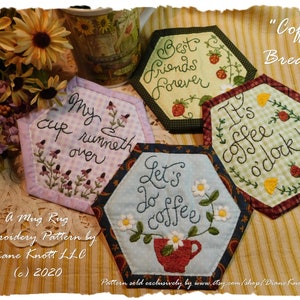 May include: A collection of four hexagonal mug rugs with embroidered designs and text. The rugs feature phrases like "My cup runneth over" and "Let's do coffee." The color palette includes pastels, with floral and coffee-themed motifs.
