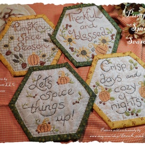 May include: Four hexagon-shaped fabric wall hangings with autumn-themed embroidery. The hangings feature the phrases "Pumpkin Spice Season", "Thankful and Blessed", "Let's Spice Things Up!" and "Crisp Days and Cozy Nights".