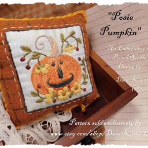 May include: A hand-stitched pillow with an embroidered pumpkin design. The pumpkin is orange with a green stem and leaves. The pillow is surrounded by a brown fabric border. The text "Posie Pumpkin" is written on a piece of paper in the background. The text "An Embroidery or Punch Needle Design by Diane Knott LLG (c) 2019" is also written on the paper. The text "Pattern sold exclusively by www.etsy.com/shop/Diane Knott LLC" is written at the bottom of the paper.