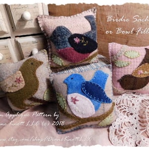 May include: Four felt applique bird sachets or bowl fillers. The birds are in various colors and designs, including blue, brown, pink, and green. The text "Birdie Sachets or Bowl Fillers" is at the top of the image.