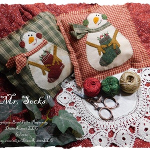 May include: Two handmade snowman-shaped fabric pillows with red and green accents. The pillows are on a red background with white polka dots. The text "Mr. Socks" is written in cursive on the image. The pillows are part of a sewing pattern for a bowl filler.