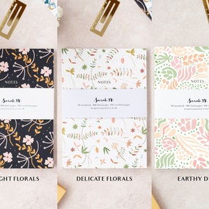 May include: Three notebooks with different floral designs. The notebooks are titled "Midnight Florals", "Delicate Florals", and "Earthy Dots". Each notebook has the text "NOTES" and "Sarah JK" printed on the front.