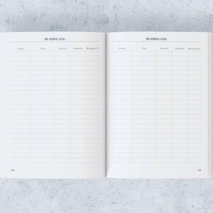 May include: Open reading log notebook with lined pages. The title "READING LOG" is printed at the top of each page. Columns are labelled for author, title, start date, finish date, and rating.