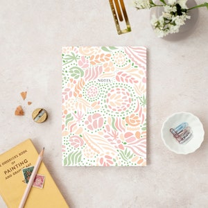 May include: A white notebook with a colorful abstract pattern in shades of pink, orange, and green. The notebook has the word "NOTES" printed on the front.