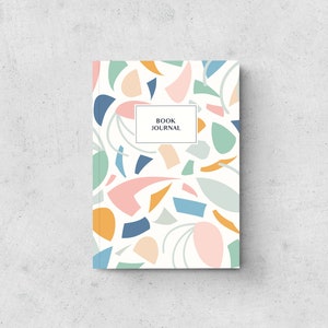May include: A hardback book journal featuring a white background and a colourful abstract pattern of shapes in blue, pink, orange, and green. The words "BOOK JOURNAL" are in a white rectangle.