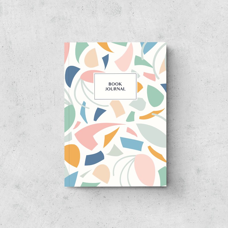 May include: A hardback book journal featuring a white background and a colourful abstract pattern of shapes in blue, pink, orange, and green. The words "BOOK JOURNAL" are in a white rectangle.