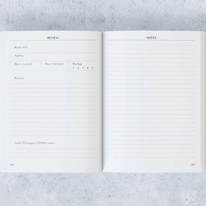May include: An open notebook with white lined pages. The left page has headings for "REVIEW" and fields for book details, including title, author, and rating. The right page is blank, with the heading "NOTES." The background is a light grey.