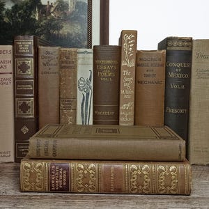 May include: A collection of vintage hardcover books in shades of brown, tan, and beige. The stack includes titles such as Raiders of Spanish Peaks, The House of the Seven Gables, The Desert of Wheat, Essays and Poems, and Conquest of Mexico.