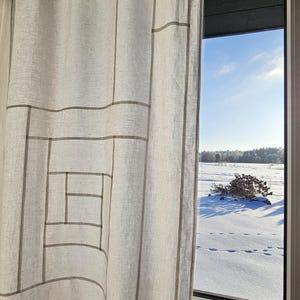Könnte beinhalten: Ein hellfarbener Leinen-Vorhang mit einem geometrischen Muster aus grauen Linien hängt vor einem Fenster. Das Fenster zeigt eine verschneite Landschaft unter einem strahlend blauen Himmel. Das Muster des Vorhangs besteht aus Rechtecken und Quadraten.