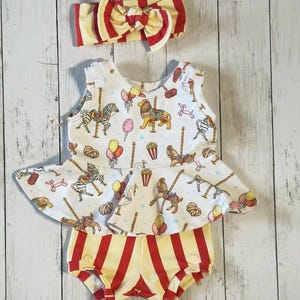 May include: A white sleeveless dress with a carousel print, red and yellow striped shorts, and a red and yellow striped headband. The dress has a ruffled bottom and the shorts are a little longer than the dress.