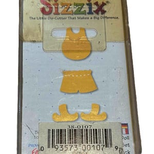 May include: A Sizzix die-cut set for doll clothing. The set includes a yellow top, shorts, and shoes. The packaging has the text "The Little Die-Cutter That Makes a Big Difference."