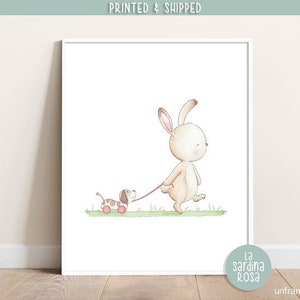May include: A watercolor illustration of a white bunny with brown ears and a brown and white puppy on a leash. The bunny is walking and the puppy is on a toy car with red wheels. The background is a green grassy field.