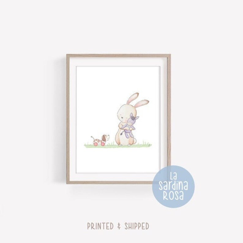 Puede incluir: Una ilustraci&oacute;n de acuarela de un conejo marr&oacute;n sosteniendo un burro morado, con un perro marr&oacute;n y blanco tirando de un carro rojo en el fondo. La ilustraci&oacute;n est&aacute; enmarcada en un marco marr&oacute;n claro.