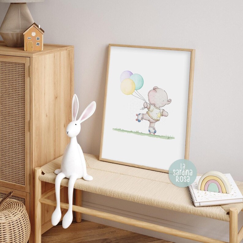Puede incluir: Una ilustraci&oacute;n de acuarela de un elefante rosa con una camisa amarilla y patines, sosteniendo tres globos en tonos de morado, verde y amarillo. La ilustraci&oacute;n est&aacute; enmarcada y colgada en una pared sobre un banco de madera.