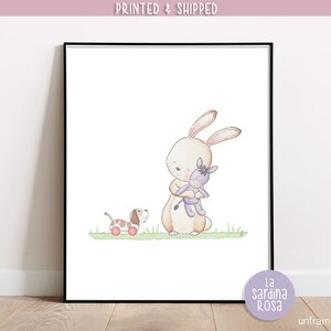 Puede incluir: Una ilustraci&oacute;n de acuarela de un conejo marr&oacute;n sosteniendo un burro de peluche morado. Un perro marr&oacute;n y blanco con ruedas rojas est&aacute; en el fondo. La ilustraci&oacute;n est&aacute; sobre un fondo blanco con un borde de hierba verde.