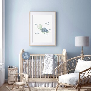 May include: A nursery room with a white crib, a rocking horse, a wicker chair, and a framed print of a green turtle swimming with blue fish. The print is on a light blue wall.